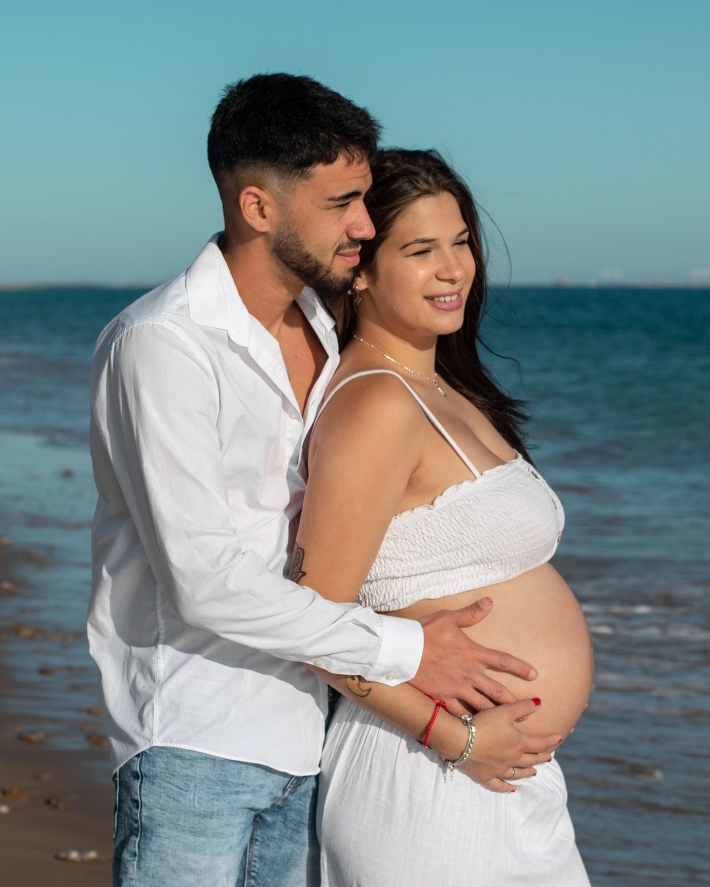 Pareja abrazada frente al mar, con la barriga